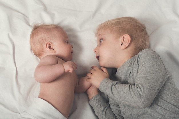 Lindo bebé y sonriente hermano mayor están acostados en la cama. Juega e interactúa. Vista superior