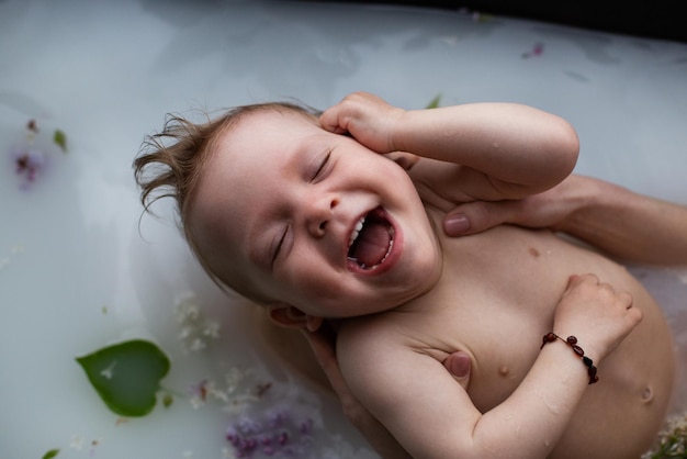 Lindo bebé sonriente con los ojos cerrados toma un baño floral de leche Madre baña suavemente a su pequeño hijo