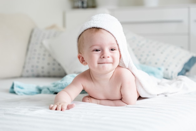 Lindo bebé sonriente en toalla con capucha arrastrándose sobre la cama después de bañarse