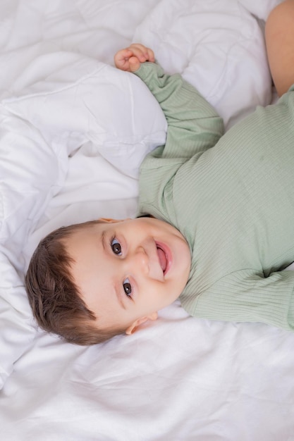 Lindo bebé sonriente en un traje de algodón verde está acostado en una cama blanca en su vista superior trasera