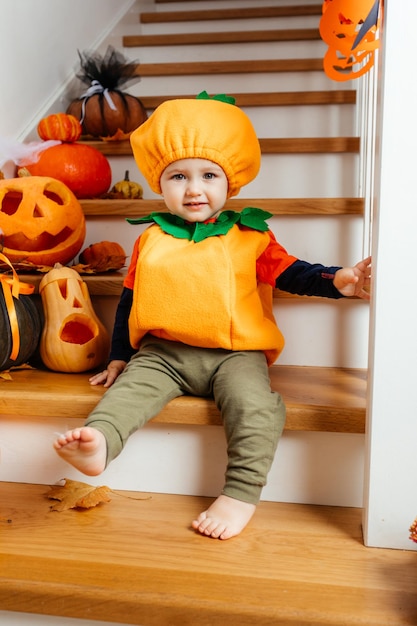 Lindo bebé sonriente vestido como calabaza mirando a la cámara