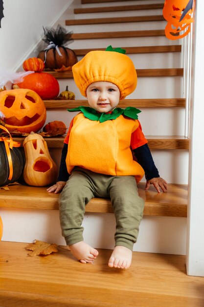 Lindo bebé sonriente vestido como calabaza mirando a la cámara