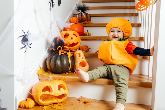 Lindo bebé sonriente vestido como calabaza mirando a la cámara