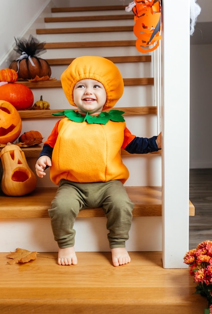 Lindo bebé sonriente vestido como calabaza mirando a la cámara