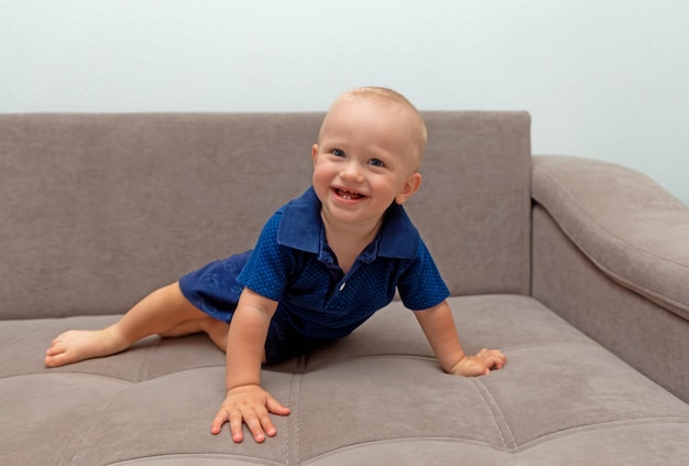 Lindo bebê sorridente em uma blusa azul e pés descalços em um sofá bege