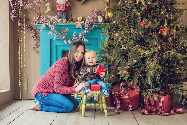 Lindo bebé con su madre sentada cerca del árbol de Navidad