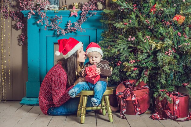 Lindo bebé con su madre sentada cerca del árbol de Navidad