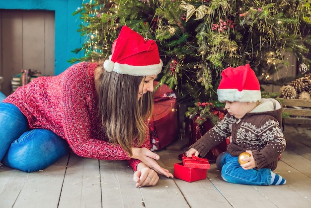 Lindo bebé con su madre sentada cerca del árbol de Navidad