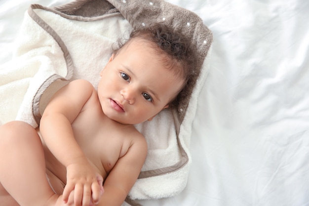Lindo bebé con toalla después de bañarse acostado en la cama en casa