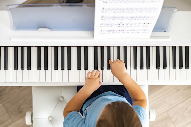 Lindo bebé tocando el piano forte eléctrico blanco presionando teclas niño estudiando en la escuela musical