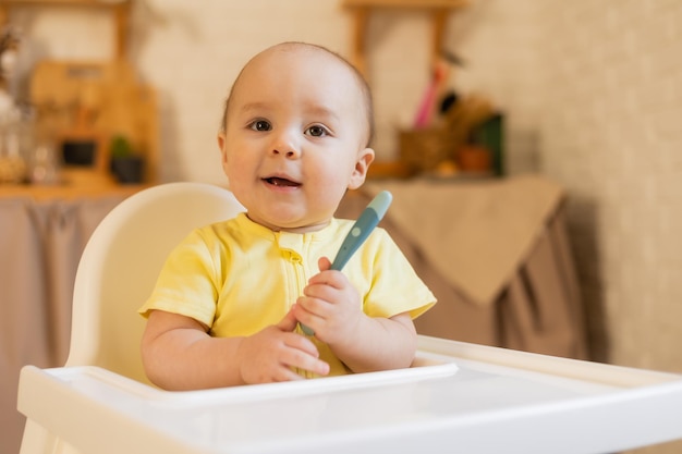 Un lindo bebé con un traje amarillo está sentado en una silla alta en la cocina de la casa con un