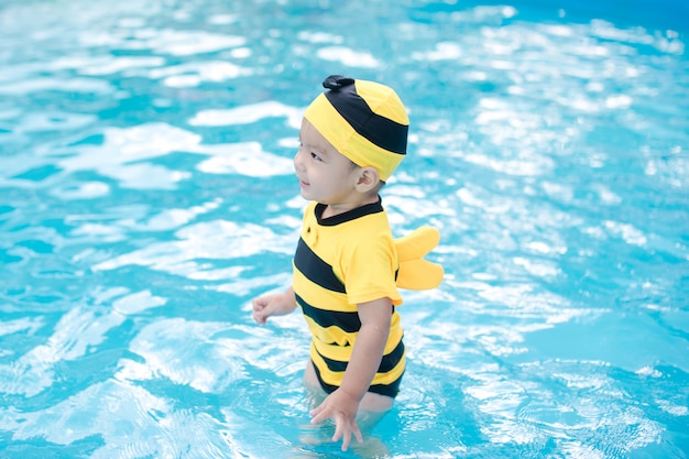 Lindo bebé en traje de baño amarillo juega en la hermosa piscina azul