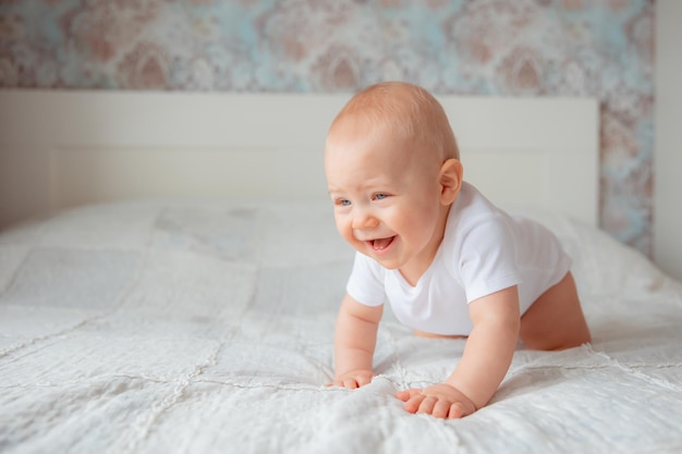 Lindo bebé con un traje blanco arrastrándose en la cama en el dormitorio el concepto de maternidad feliz