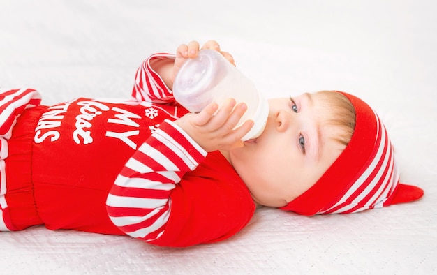 Lindo bebé con traje de navidad comiendo leche de botella estilo de vida y concepto de vacaciones de invierno