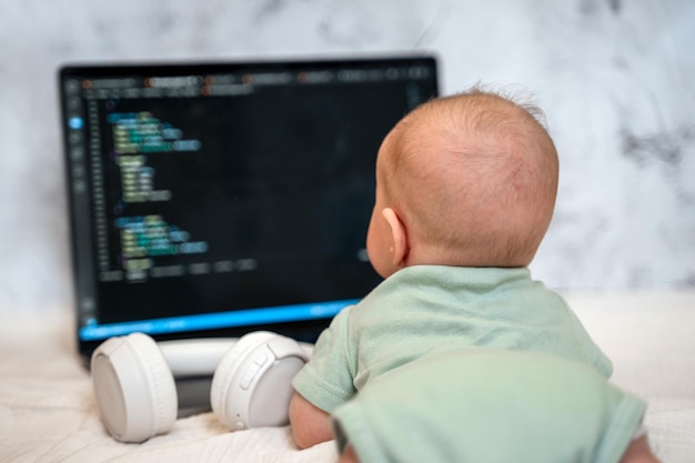 Un lindo bebé de tres meses está acostado frente a una computadora portátil. Un concepto divertido de un programa para niños de negocios