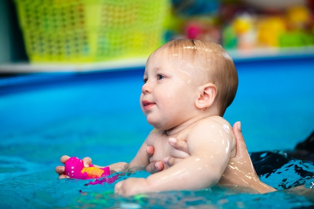 Lindo bebé triste aprendiendo a nadar en una piscina especial para niños pequeños. Actividades para niños. Ejercicios con entrenador