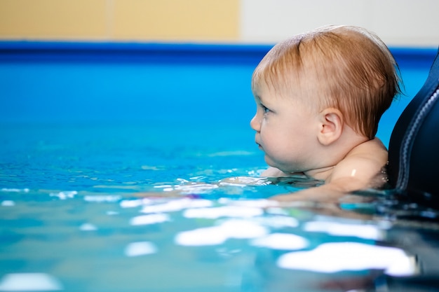 Lindo bebé triste aprendiendo a nadar en una piscina especial para niños pequeños