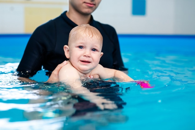 Lindo bebé triste aprendiendo a nadar en una piscina especial para niños pequeños