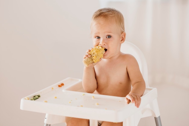 Foto lindo bebé en trona comiendo maíz solo