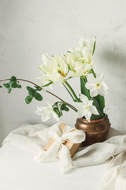 Lindo buquê branco com caixa de presente na mesa de madeira contra a parede rústica feliz dia das mães elegante primavera tulipas e narcisos em vaso vintage e presente dia das mulheres espaço para texto