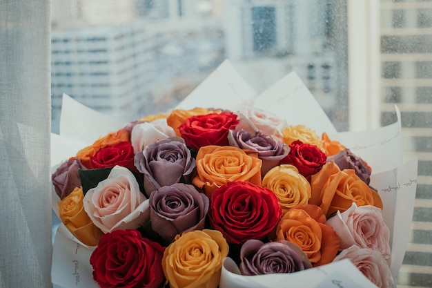 Lindo buquê de arranjo de rosas naturais coloridas com papel de embrulho na frente da janela