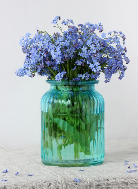 Lindo buquê de esquecimentos azuis em um vaso de vidro flores delicadas em um fundo claro