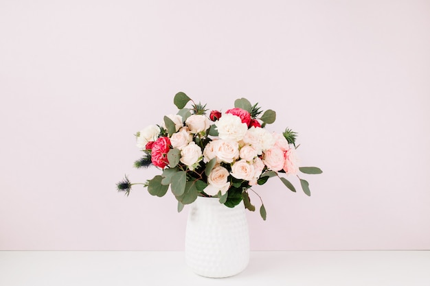 Lindo buquê de flores em um vaso de flores perto de uma parede rosa pastel