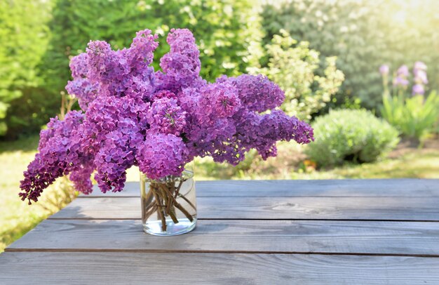 Foto lindo buquê de flores lilás roxas em uma jarra de vidro em uma mesa de madeira no jardim