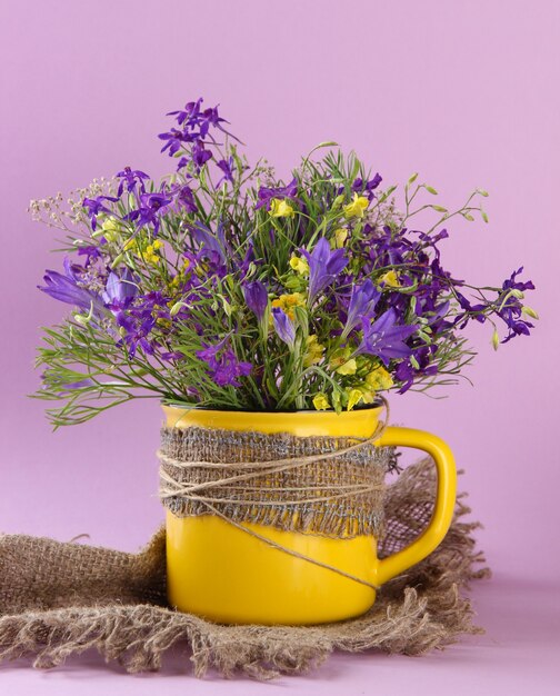 Lindo buquê de flores silvestres na xícara em fundo roxo