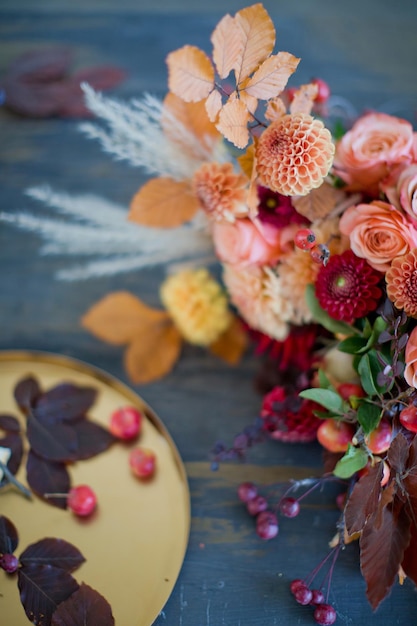 Lindo buquê de outono com flores e bagas laranja e vermelhas Buquê de outono e bandeja dourada com pequenas maçãs em uma mesa de madeira