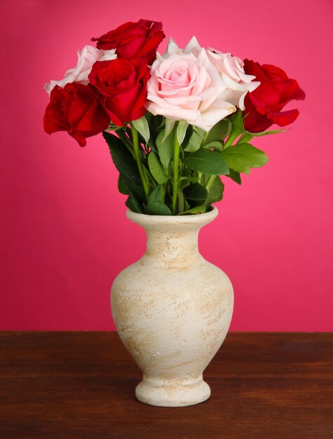 Foto lindo buquê de rosas em um vaso com o presente na mesa no fundo rosa