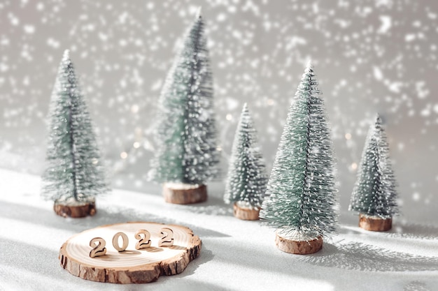 Lindo cartão de ano novo. Números decorativos 2022 no suporte de madeira e pinheiros verdes no fundo desfocado cinza com neve. Feliz ano novo de 2022.