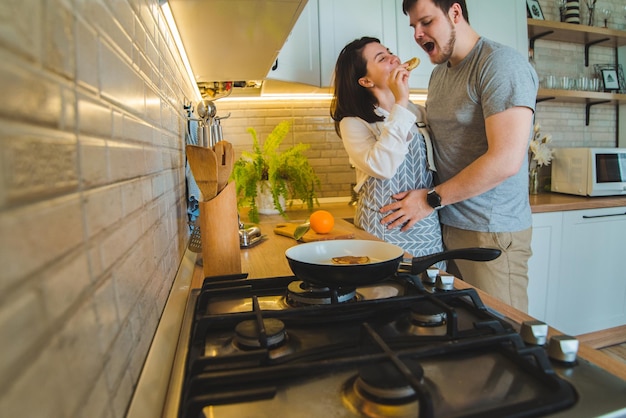 Lindo casal abraçando na cozinha enquanto cozinha o café da manhã