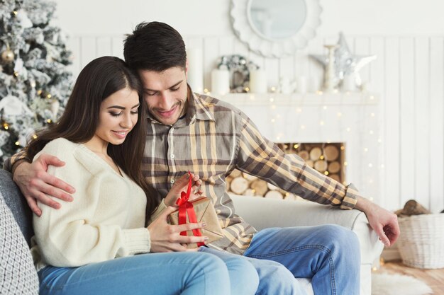 Lindo casal abrindo presentes de natal, sentado na sala de estar, comemorando juntos as férias de inverno, copie o espaço