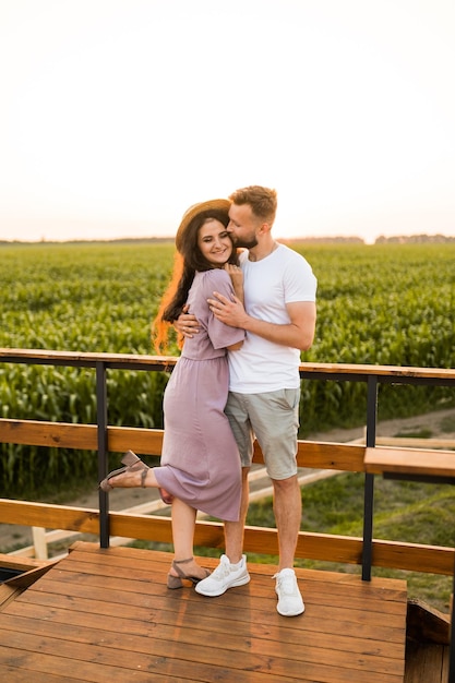 Lindo casal alegre em pé no campo abraçando tendo um encontro no pôr do sol aproveitando momentos para