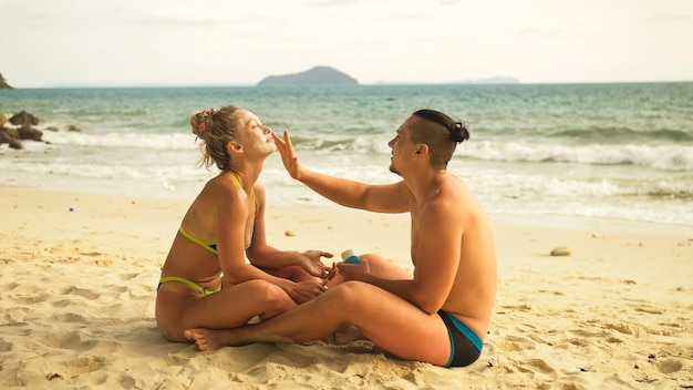 Lindo casal amoroso um ao outro com protetor solar Mulher para colocar protetor solar Jovem garota e cara cara a cara usando protetor solar Conceito resto tropical resort viajando turismo feliz férias de verão