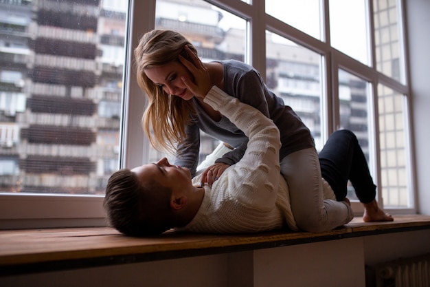 Lindo casal apaixonado abraçando e se diverte em seu quarto perto da janela