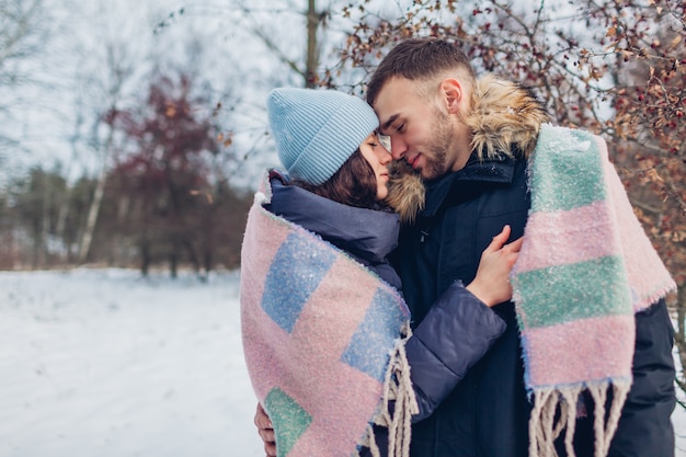Lindo casal apaixonado andando e abraçando na floresta de inverno. Pessoas aquecimento coberto com manta