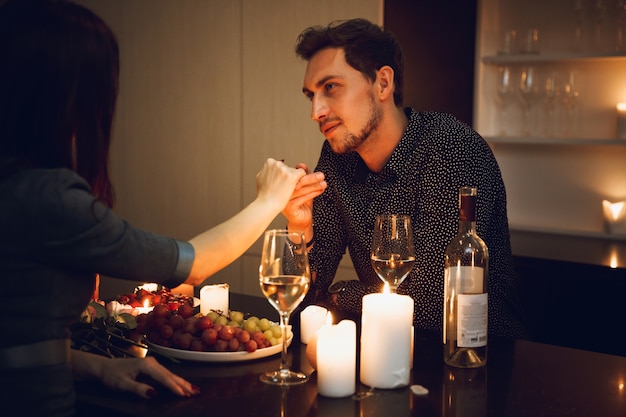 Lindo casal apaixonado em um jantar romântico à luz de velas em casa, homem beijando a mão