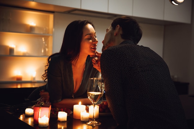 Lindo casal apaixonado jantando à luz de velas em casa, bebendo vinho, brindando, beijando