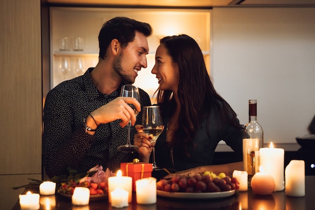 Lindo casal apaixonado jantando à luz de velas em casa, bebendo vinho, brindando