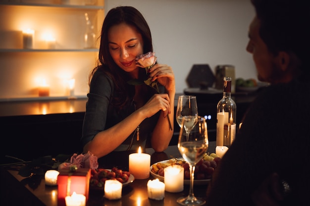 Lindo casal apaixonado jantando à luz de velas em casa, mulher cheirando uma flor