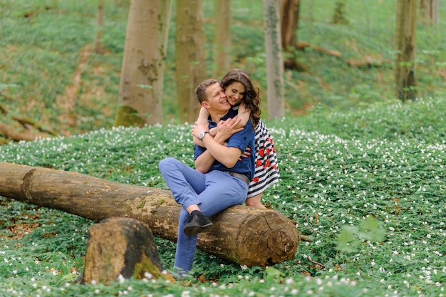 Lindo casal apaixonado na floresta. um homem senta-se em uma árvore derrubada. uma mulher o abraça por trás. espaço livre.