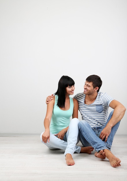 Lindo casal apaixonado sentado no chão em uma sala em fundo cinza