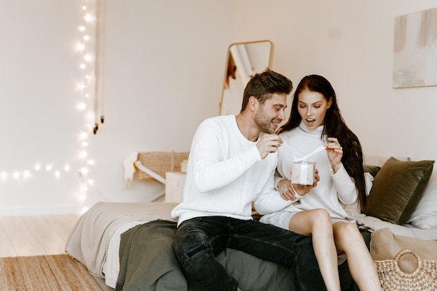 lindo casal apaixonado troca presentes enquanto está sentado no sofá em casa abrindo caixas com presentes românticos para o dia dos namorados ou aniversário