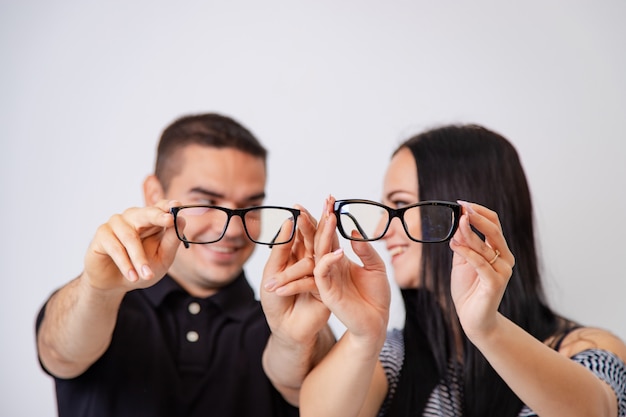 Lindo casal atraente sentados juntos e olhando um ao outro segura os óculos nas mãos. Jovem casal sorrindo um ao outro mostra óculos