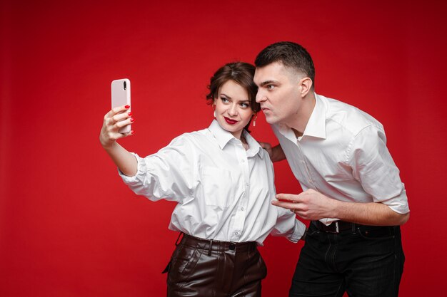 Lindo casal caucasiano apaixonado toma selfie e se diverte muito, imagens isoladas na parede vermelha