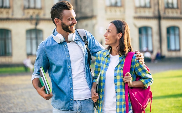 Lindo casal com mochilas depois das aulas na universidade está se abraçando e caminhando ao ar livre.