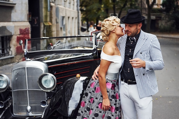 Lindo casal com roupas antiquadas está na cidade com um carro retrô.