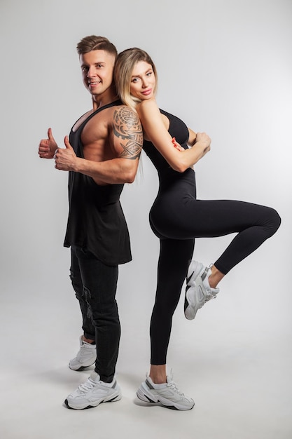 Lindo casal de esportes feliz posando no estúdio em um fundo branco Linda garota fitness magro e homem bonito musculoso em roupas esportivas pretas com tênis